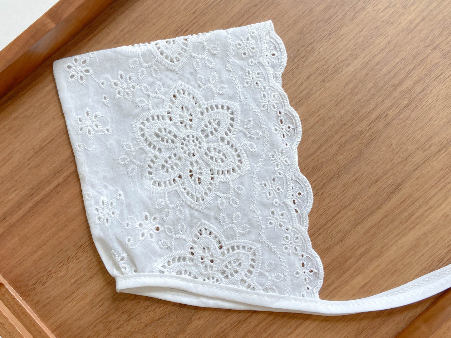 Baby bonnet is made from embroidered white cotton fabric with eyelets and has ties.  Bonnet features embroidery with dahlia flower and a chevron edge. The flower embroidered on the bonnet has six petals and pointed edges. 